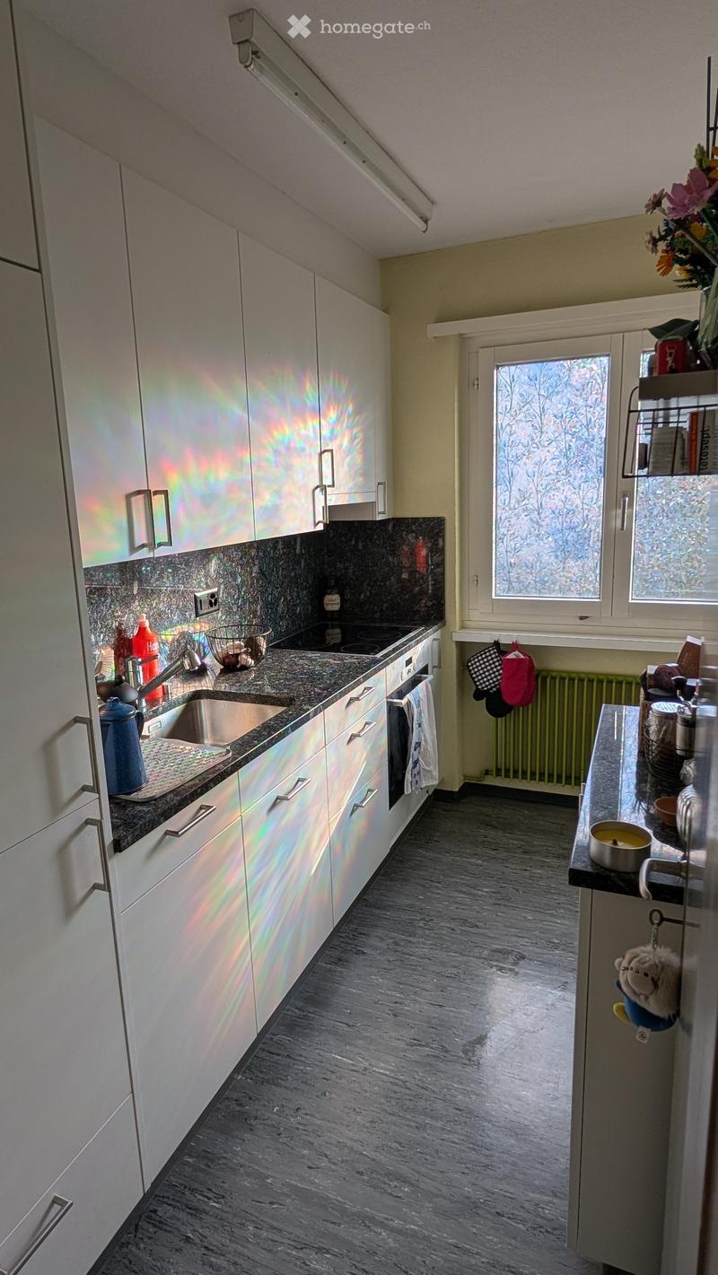 Modern kitchen with white cabinets, granite countertops, stainless steel sink, and various appliances including an oven and refrigerator. The space features a window with frosted glass and a radiator below it.