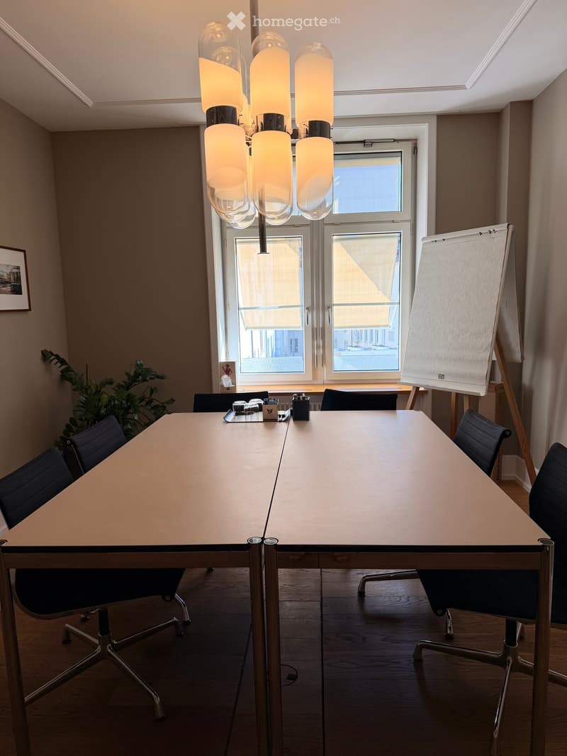 Modern conference room with a large rectangular table, several chairs, a hanging lamp, and a large screen on a stand.