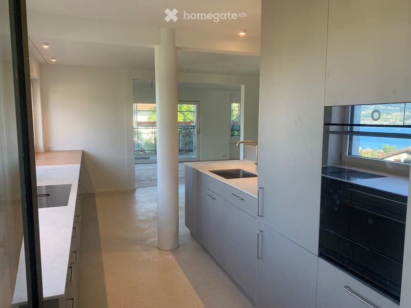 Modern kitchen with white cabinets, light countertops, and a sink with a modern faucet. Large windows offer a scenic view.