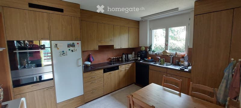Bright kitchen with light wooden cabinets, stainless steel appliances, and a dining area with a wooden table and chairs.