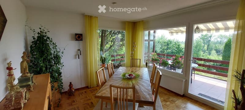 Bright dining room with wooden floor, large windows, yellow curtains, dining table with chairs, decorative statues, and vases.
