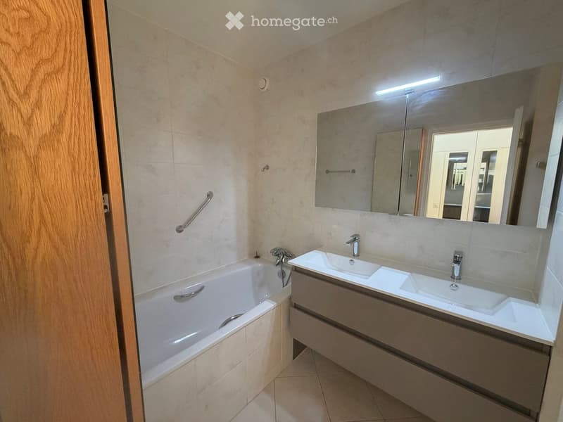 Modern bathroom with a bathtub, double sink, large mirror, and built-in storage cabinet.