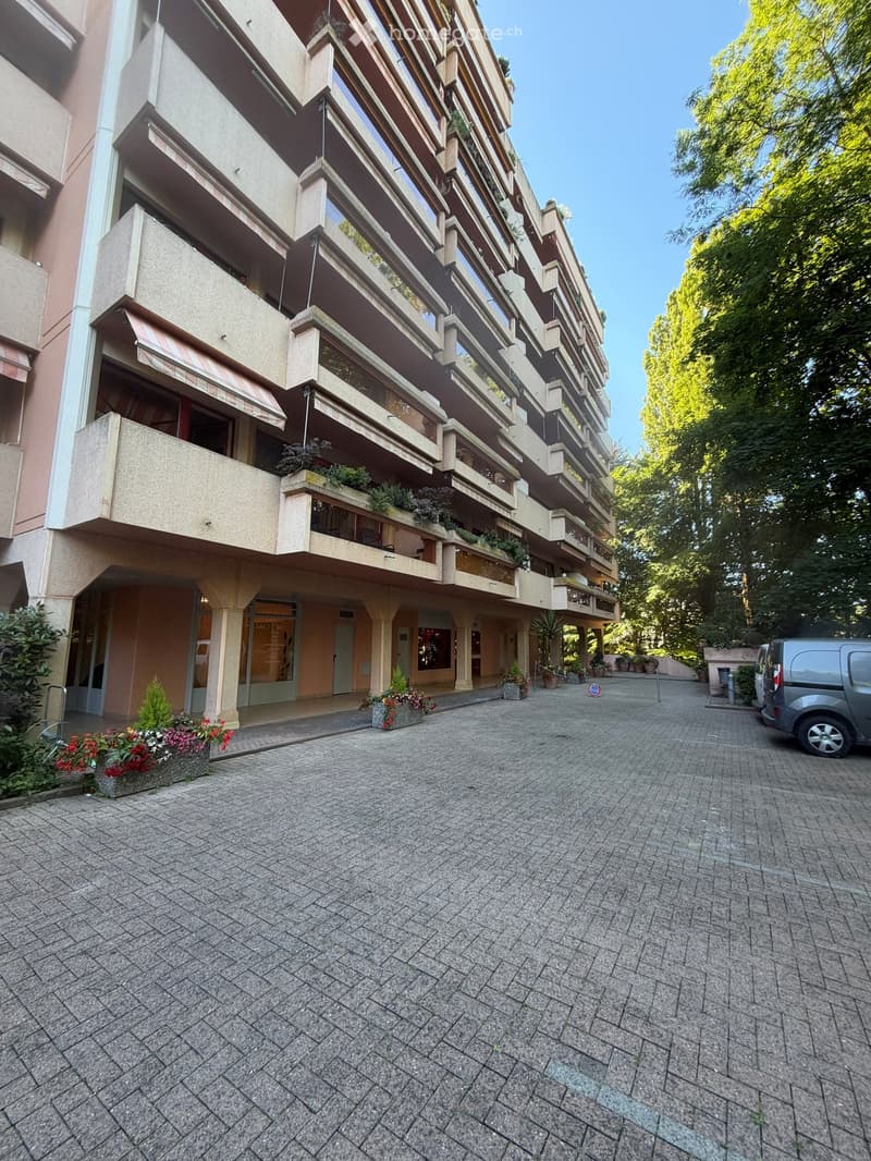 Multi-story residential building with balconies, potted plants, and a paved courtyard.