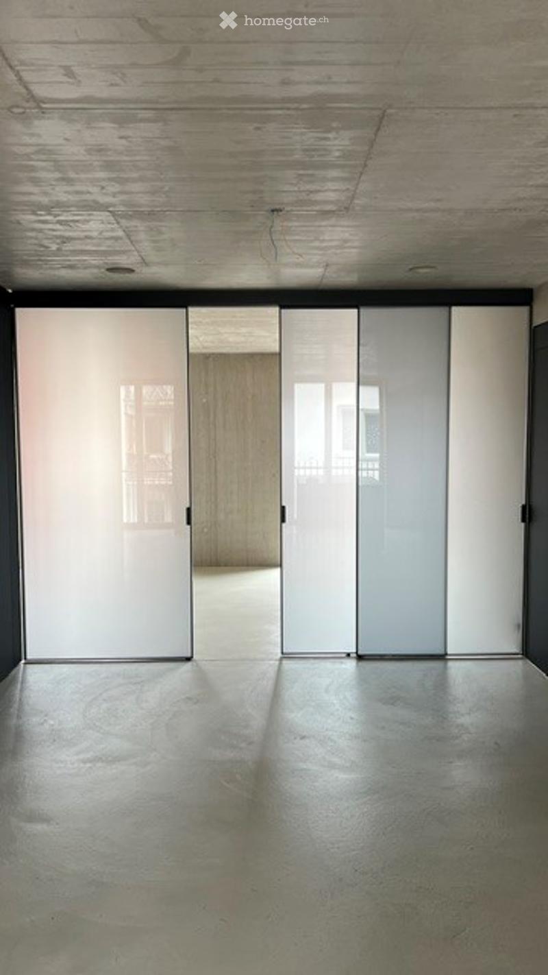 Empty room with polished concrete floor, white sliding doors, and exposed wooden ceiling beams.