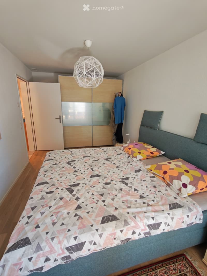 Cozy bedroom with a modern bed, geometric-patterned duvet, colorful pillows, a sleek wardrobe, and a hanging geometric lamp.
