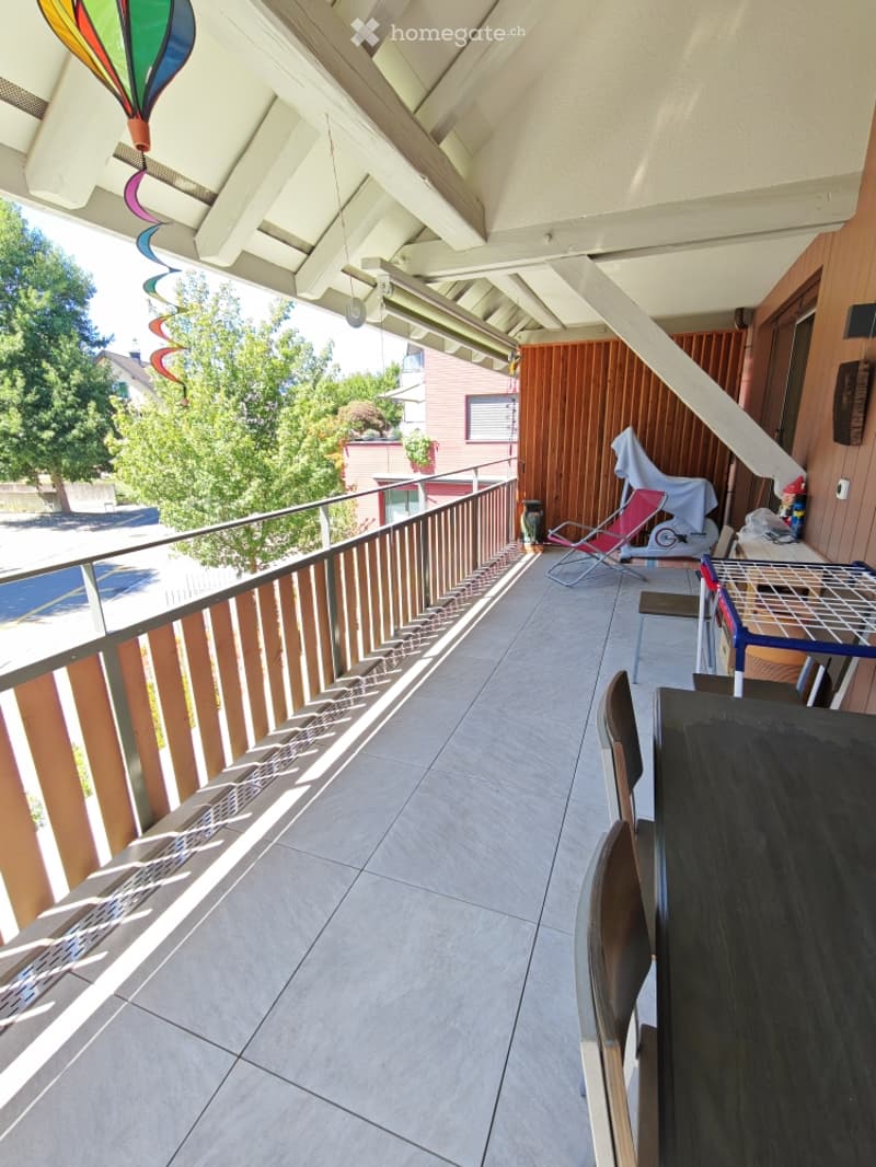 Balcony with tiled floor, wooden railing, and outdoor furniture including a table and chairs.