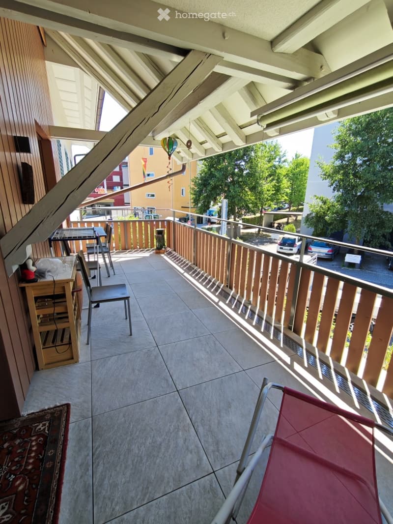 Balcony with tiled floor, wooden railing, and outdoor furniture including a table, chairs, and a small shelf.