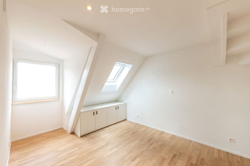 Bright, empty attic room with wooden flooring, white walls, built-in cabinetry, and skylight windows.