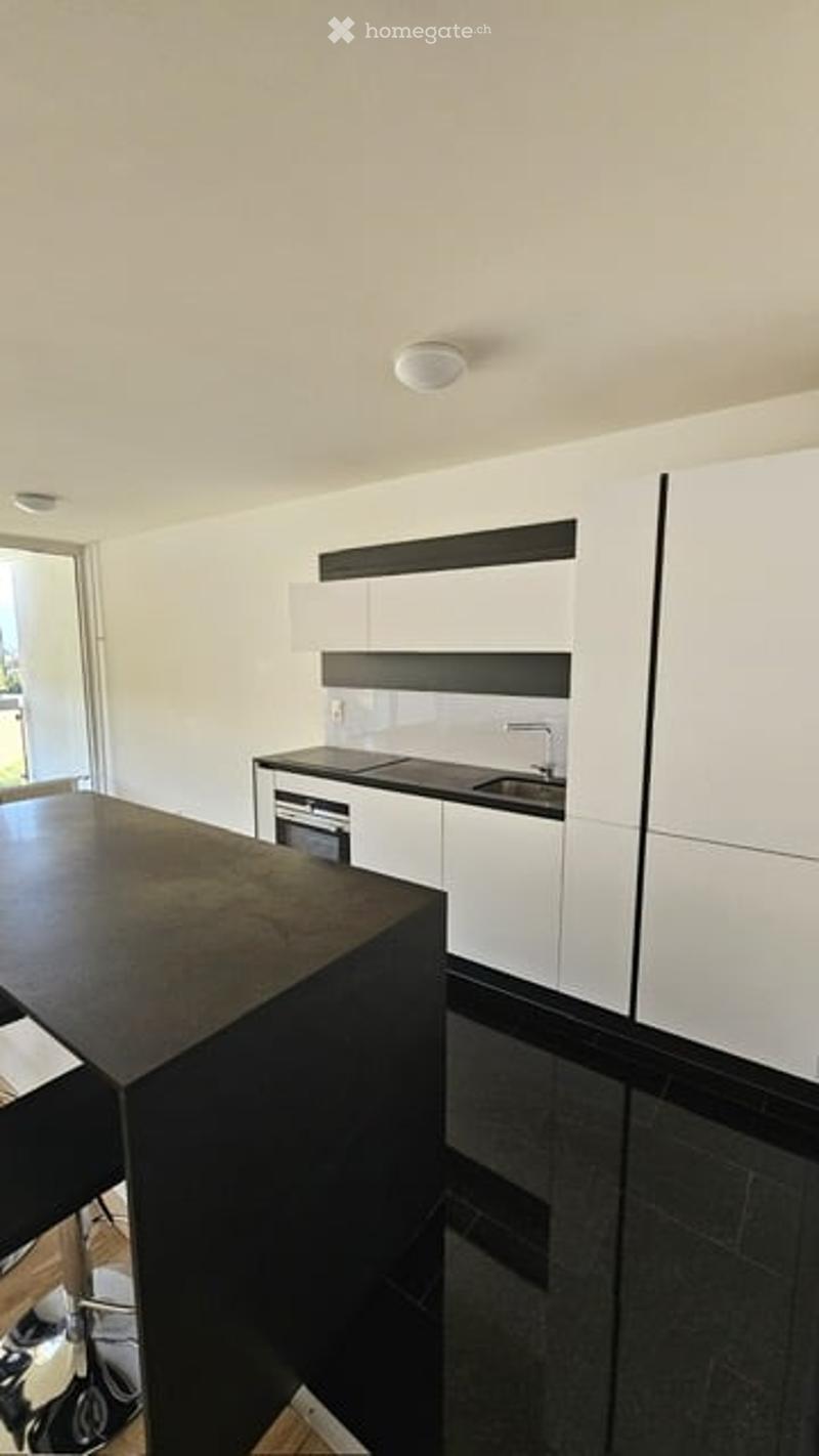 Modern kitchen with white cabinets, black countertops, and a central island table. Features a sink, faucet, and built-in oven.