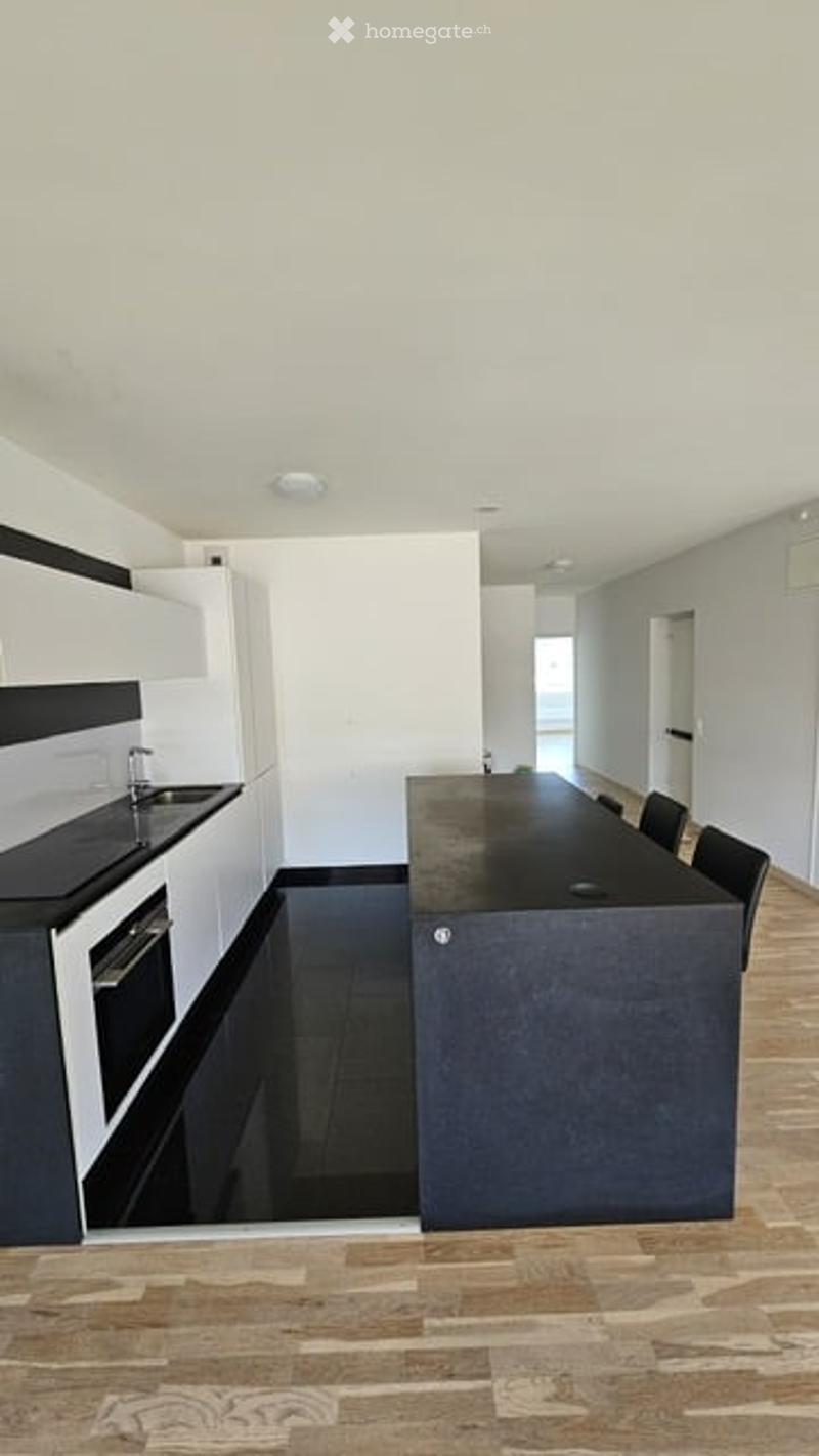 Modern kitchen with white cabinets, black countertops, and a central island with seating. Features a stove, sink, and sleek design.