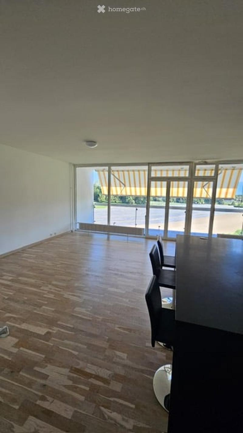 Modern, minimalist room with wooden flooring, large windows, and a balcony. Includes a stool, chair, and table.