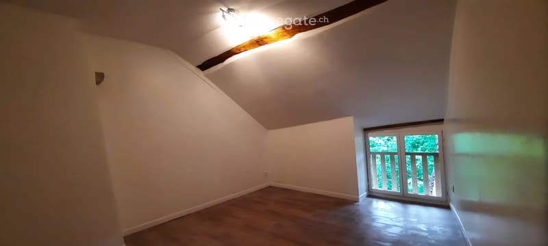 Empty room with wooden flooring, white walls, and a large window with a view of greenery outside.