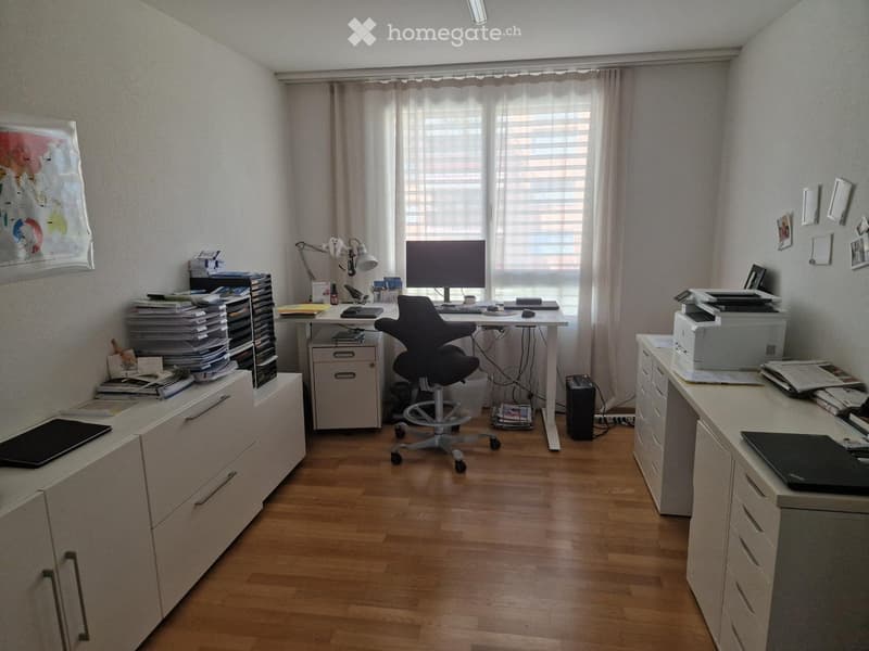 A well-organized office with a wooden floor, large window with blinds, desk with computer, chair, printer, and filing cabinets.