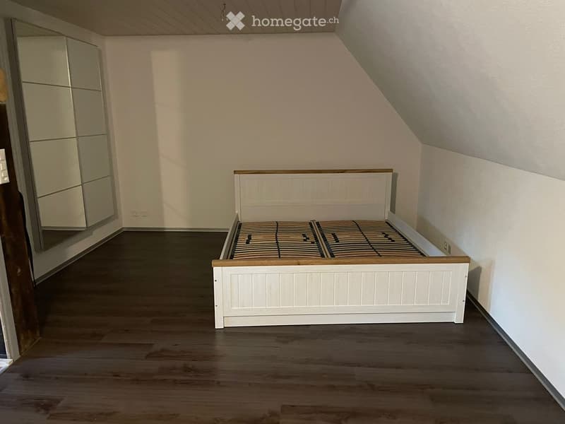 Bedroom with a white wooden bed frame and mattress, a large mirrored wardrobe, and wooden flooring.