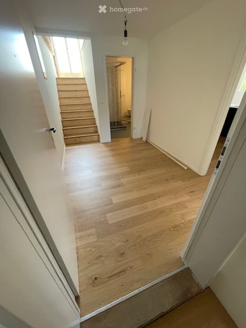 Empty hallway with wooden flooring, white walls, and a staircase leading to another room.