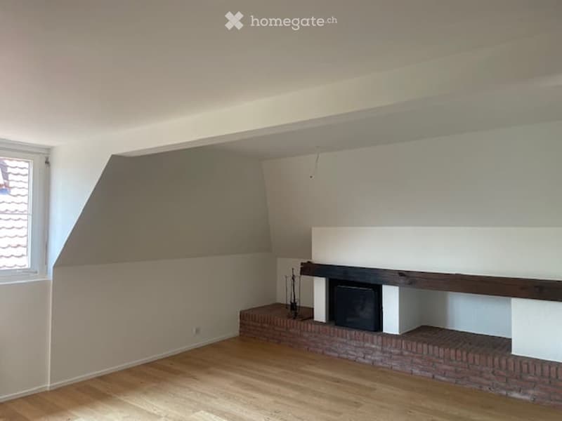 Empty room with wooden flooring, white walls, and a fireplace with a brick surround.