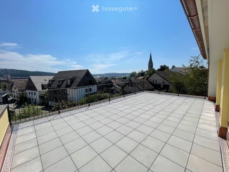 Spacious balcony with tiled floor, metal railing, and scenic view of the town and surrounding landscape.