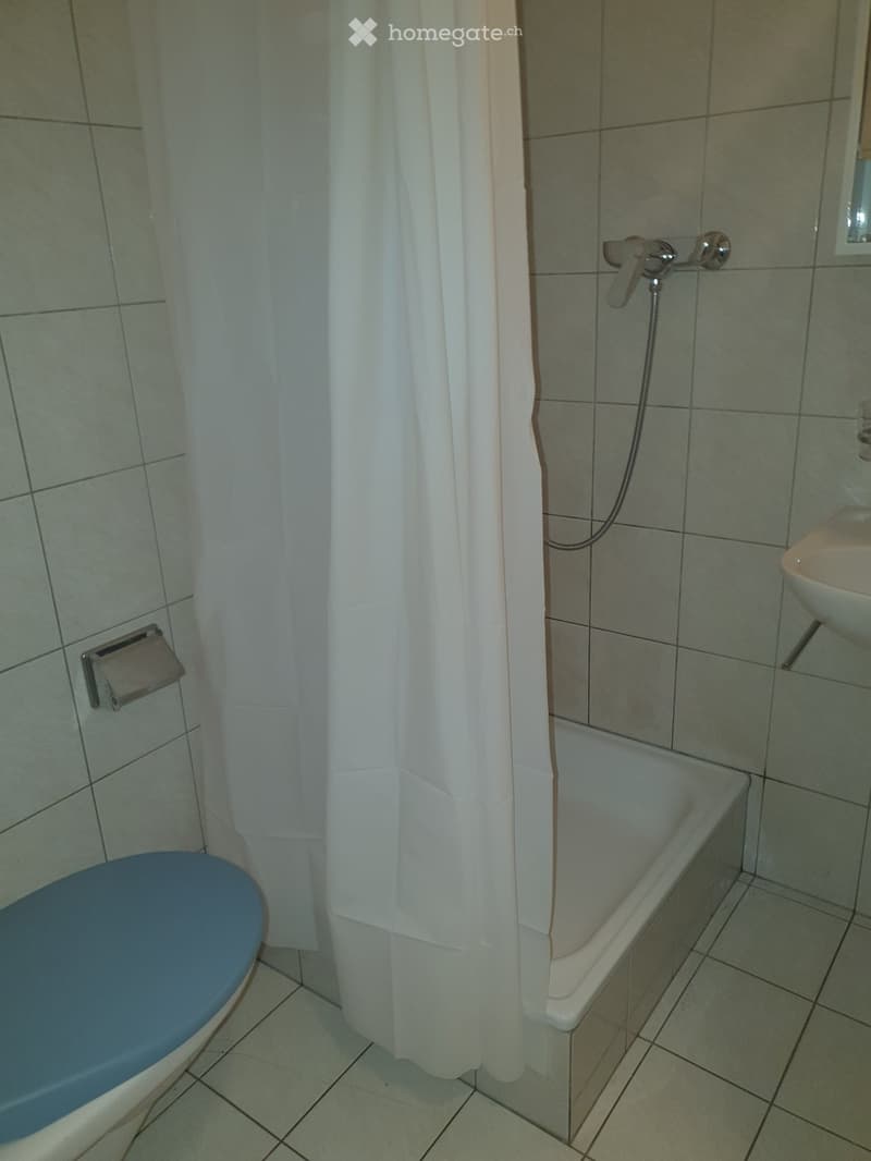 Bathroom with a bathtub, toilet, sink, and a shower curtain. The walls and floor are tiled.