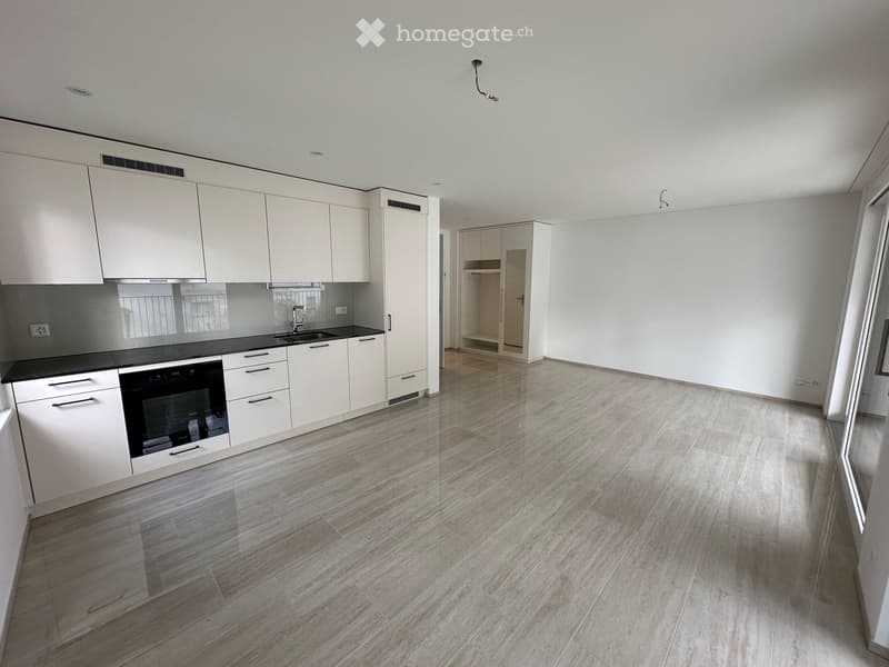 Modern kitchen with white cabinets, a black countertop, and a built-in oven. The floor is made of polished wood tiles, and the space is well-lit with recessed lighting.
