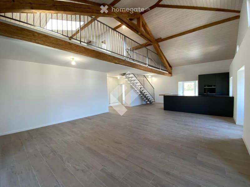 Open-plan space with wooden beams, a staircase leading to an upper level, and a modern kitchen area with dark cabinets and a countertop.