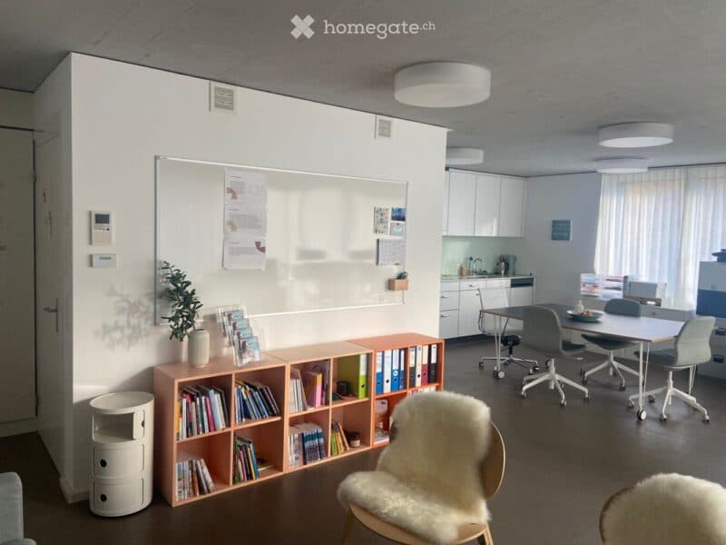 Modern office space with a mix of seating, a whiteboard, bookshelves, filing cabinets, and a small kitchenette area.