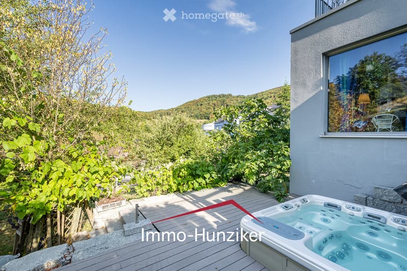 Outdoor area with a wooden deck, hot tub, lush greenery, and scenic hillside view.