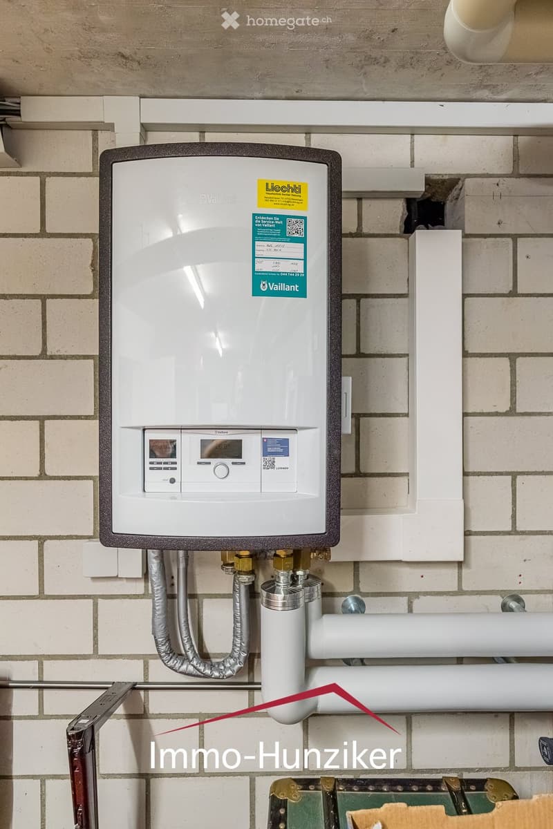 A modern Vaillant water heater unit mounted on a tiled wall, with control panel, digital display, and connected pipes.