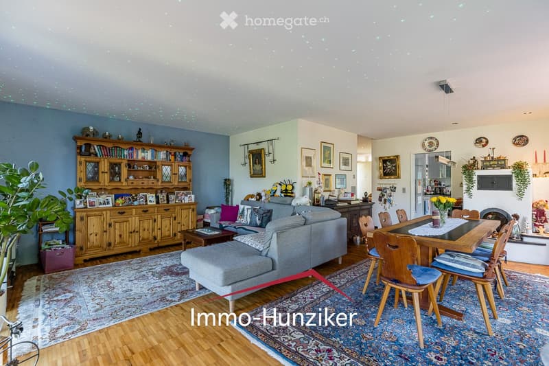 A spacious living and dining area with a grey sofa, ottoman, coffee table, wooden cabinet, bookshelf, dining table with chairs, and decorative items including vases and picture frames.