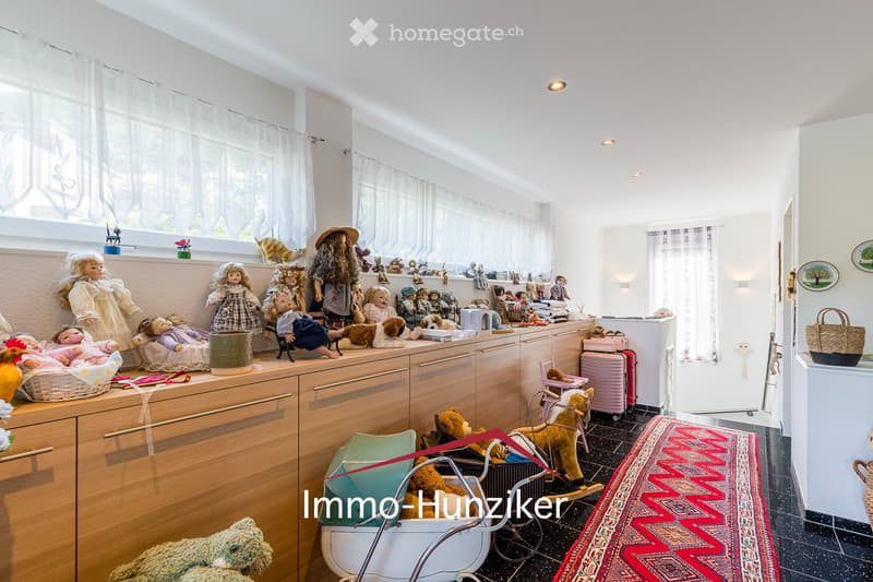 A well-lit room with wooden cabinets, a variety of dolls and toys, a baby stroller, and a basket on the floor.