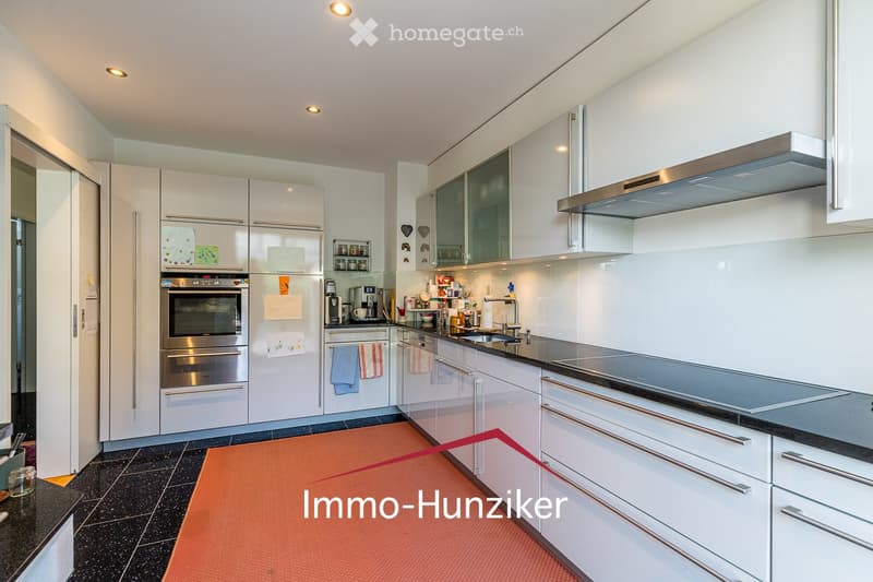 Modern kitchen with white cabinets, stainless steel appliances, and a black countertop. Features include a refrigerator, oven, dishwasher, sink, and various small appliances on the counter.