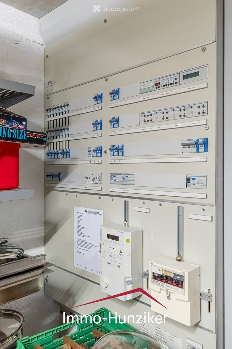 Electrical panel with multiple circuit breakers, switches, and meters mounted on a wall.