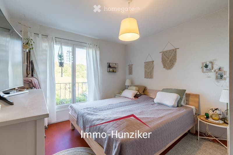 Cozy bedroom with a double bed, nightstands, wall hangings, and a view through large windows.
