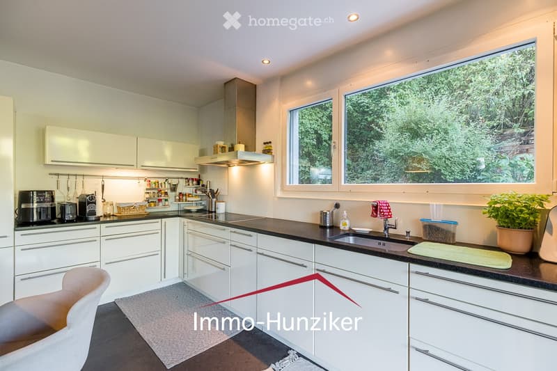 Modern kitchen with white cabinets, black countertops, stainless steel appliances, and large windows overlooking greenery.