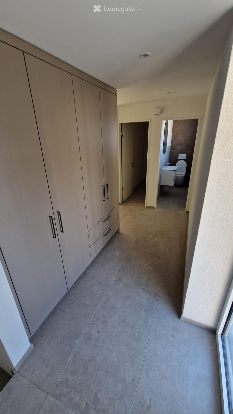 Empty hallway with beige tiled flooring, white built-in storage units on one side, and an open doorway leading to a bathroom.