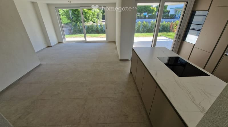 Empty room with tiled floor, white walls, large glass doors leading to outdoor area, and a modern kitchen island with built-in sink.
