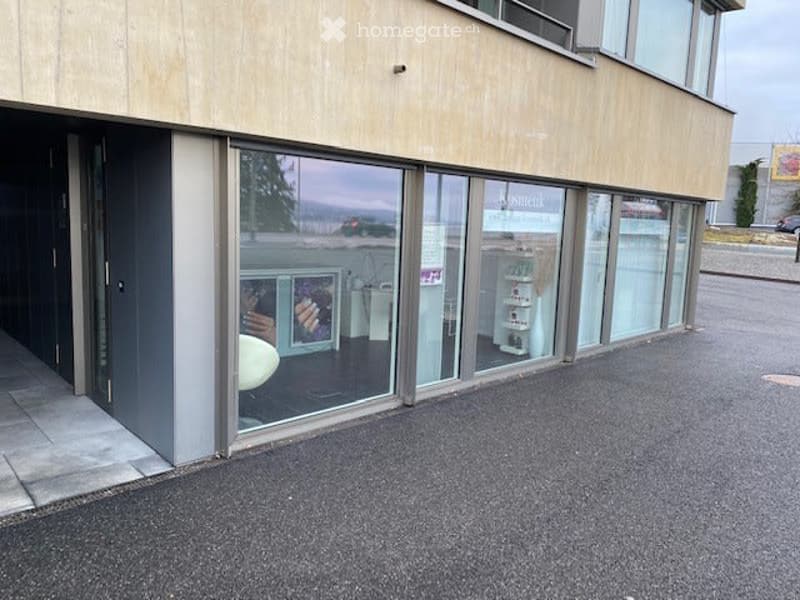Modern commercial building with large glass windows and a clean, contemporary design. The entrance features a dark door and a small covered area.