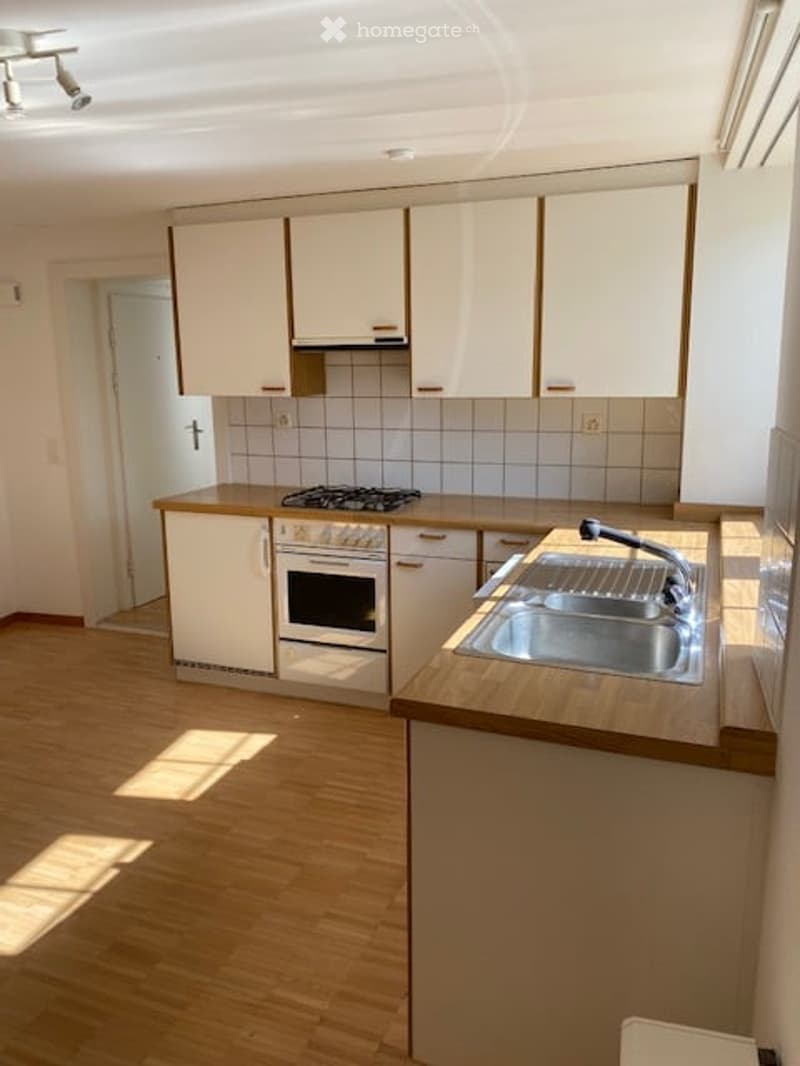 Modern kitchen with white cabinets, wooden countertops, stainless steel sink, and built-in oven. Light wooden flooring and tiled backsplash.