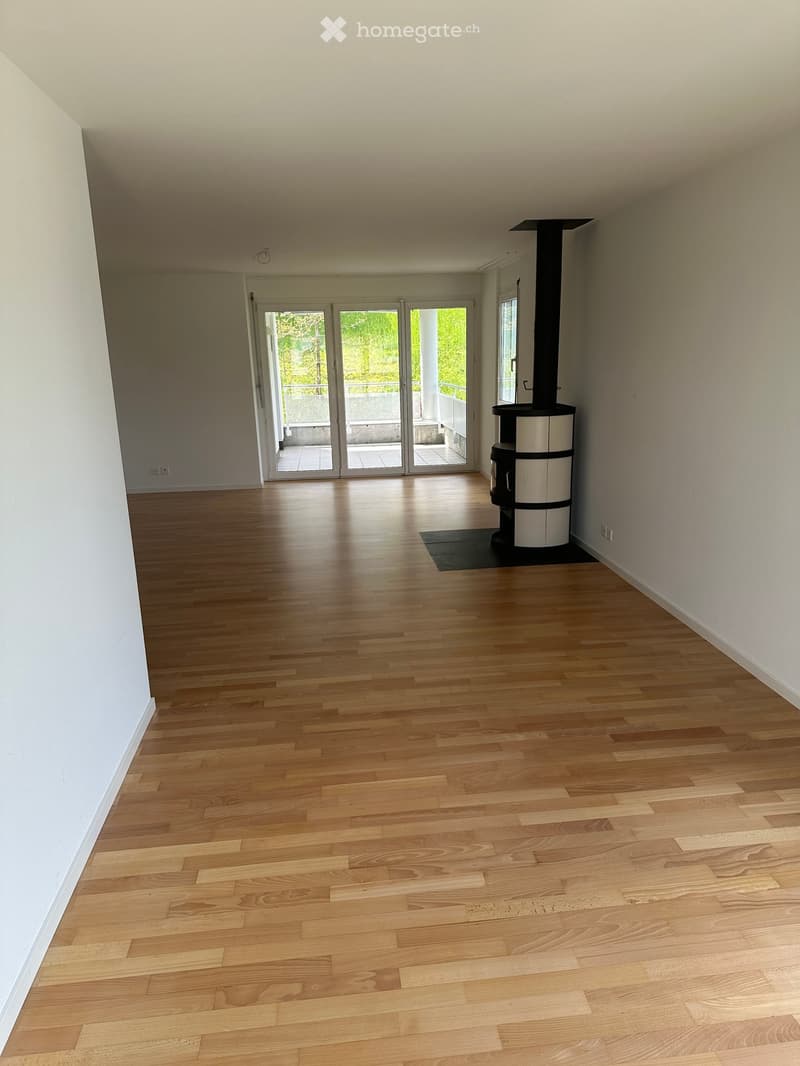Empty room with light wooden flooring, white walls, and a modern fireplace in the corner. Large glass doors lead to a balcony area.