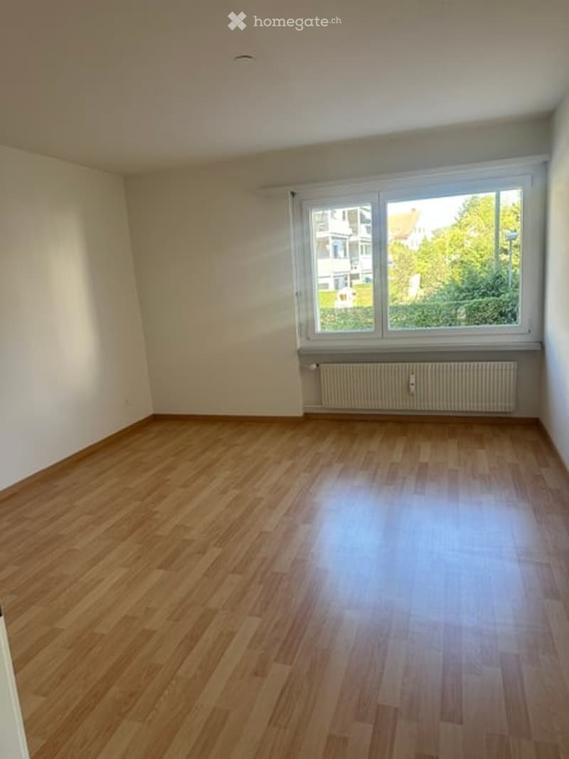 Empty room with wooden flooring, white walls, and a large window with a radiator below it.