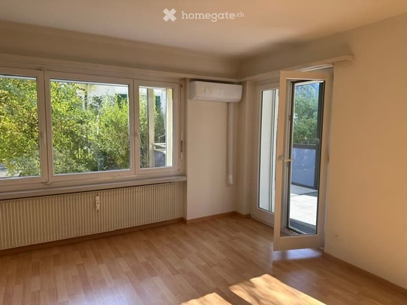 Empty room with wooden flooring, large windows, and an open sliding door leading to a balcony.