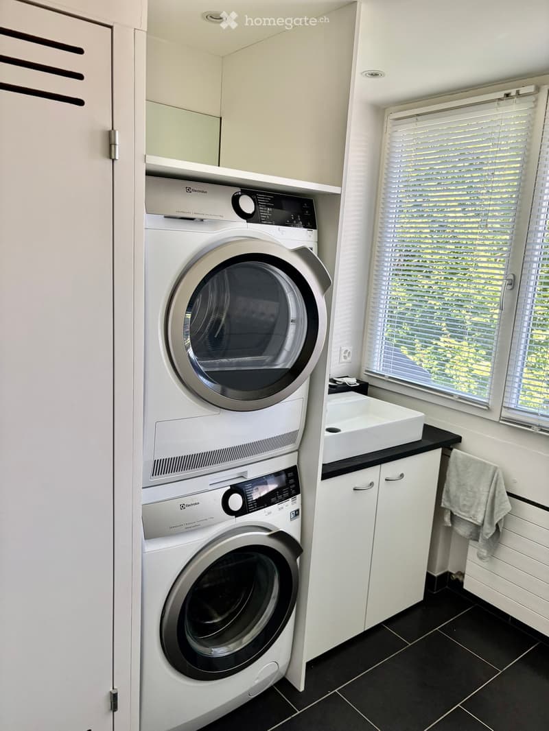 Modern bathroom with a stacked washer and dryer unit, a white sink, and a towel hanging on the side.