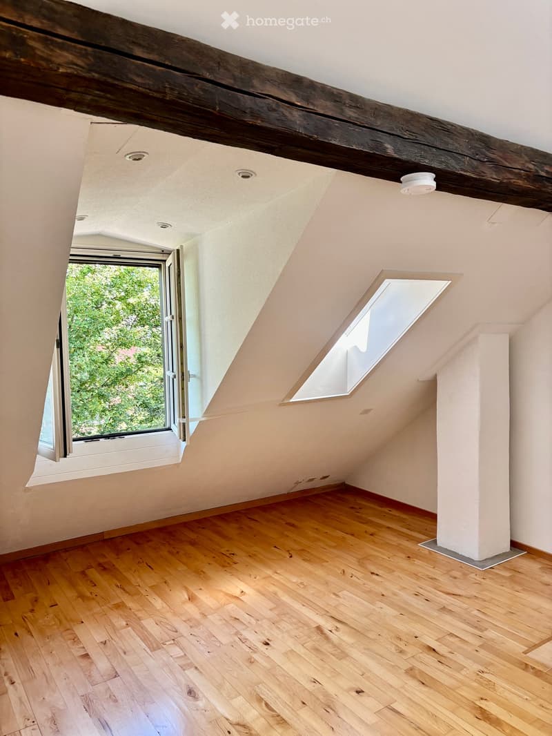 Empty attic room with wooden flooring, exposed wooden beams, skylight windows, and a large opening to the outside.