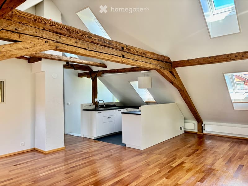 Bright, modern kitchen with wooden flooring, white cabinets, and exposed wooden beams. Features a sink, faucet, and a countertop.
