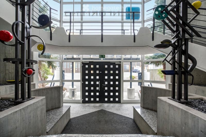 Modern, minimalist hallway with large glass windows, black double doors, and abstract metal sculptures on either side.
