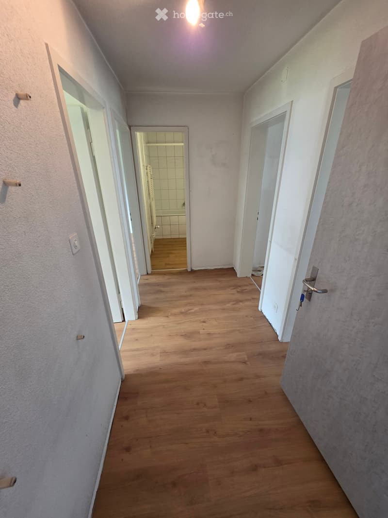 Empty hallway with wooden flooring, white walls, and several doors leading to other rooms.