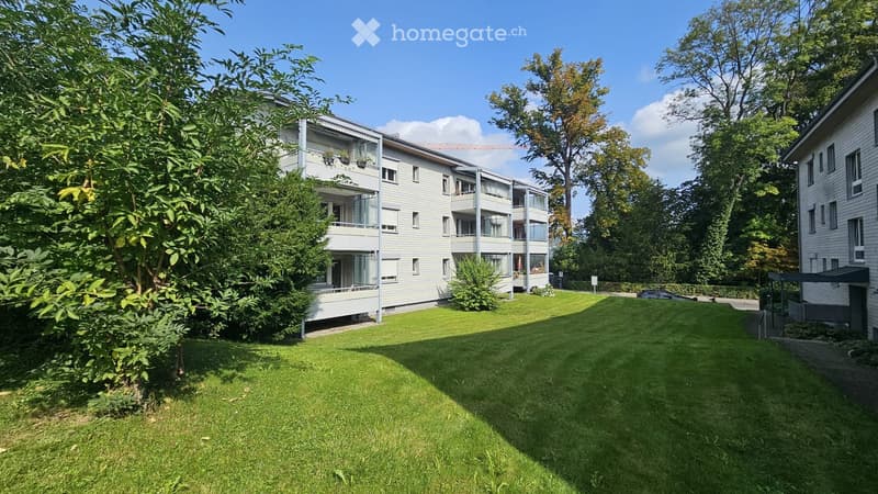 Apartment building with balconies, surrounded by trees and grass