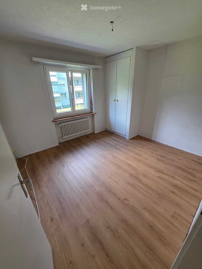 Empty room with wooden flooring, white walls, a window with a radiator below, and a white closet.