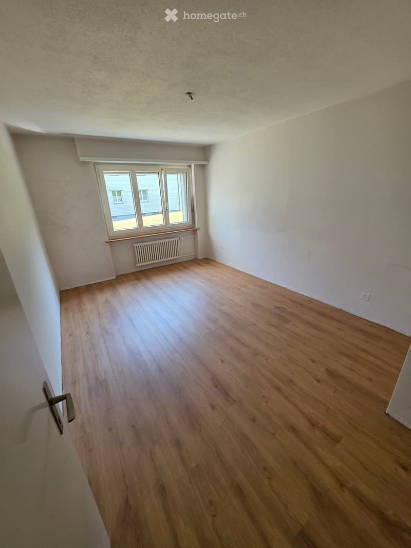 Empty room with wooden flooring, white walls, and a window with a radiator below it.