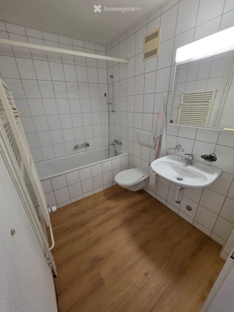 Bathroom with wooden floor, white tiled walls, bathtub, toilet, sink, and radiator.
