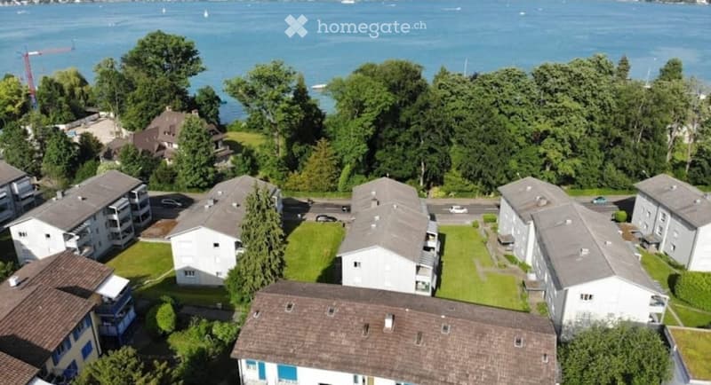 Aerial view of a residential complex with multiple buildings, green lawns, and a scenic lake view in the background.